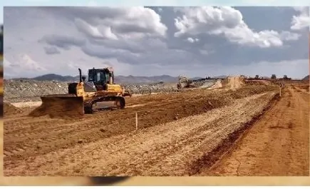 Trator de esteira nivelando aterro, com serra e céu nublado ao fundo