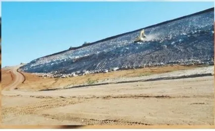 Talude de barragem revestido com manta escura, sob céu azul