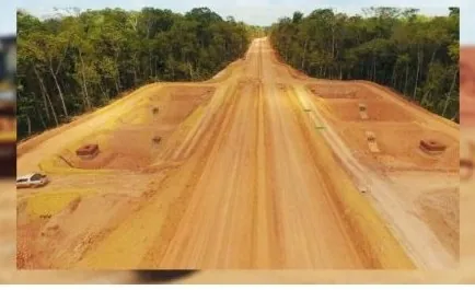 Estrada de terra larga e reta aberta em meio à floresta