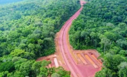 Vista aérea de estrada de terra vermelha aberta em meio à floresta, com pátios laterais