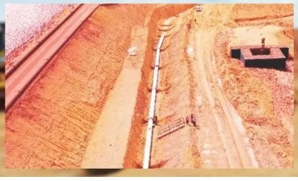 Vista aérea de canal escavado com tubulação assentada ao longo do talude e caixa de concreto ao lado