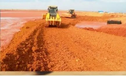 Tratores de esteira espalhando solo vermelho em frente de aterro