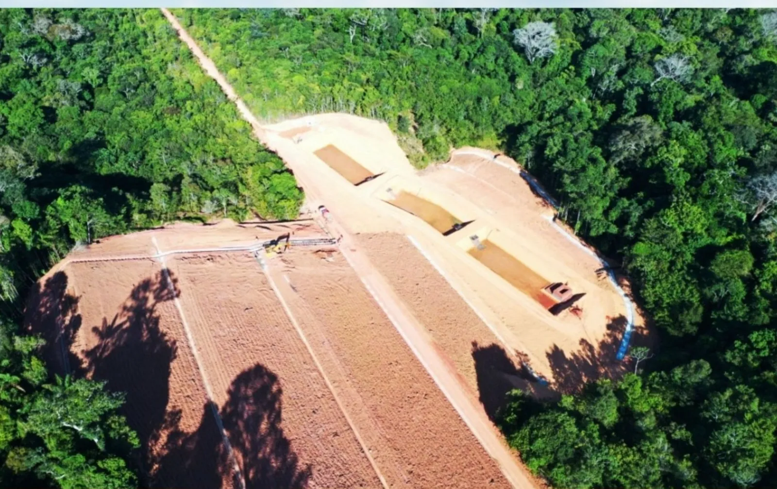 Vista aérea de clareira aberta na floresta, com terreno em conformação, linhas de drenagem e caminho de serviço